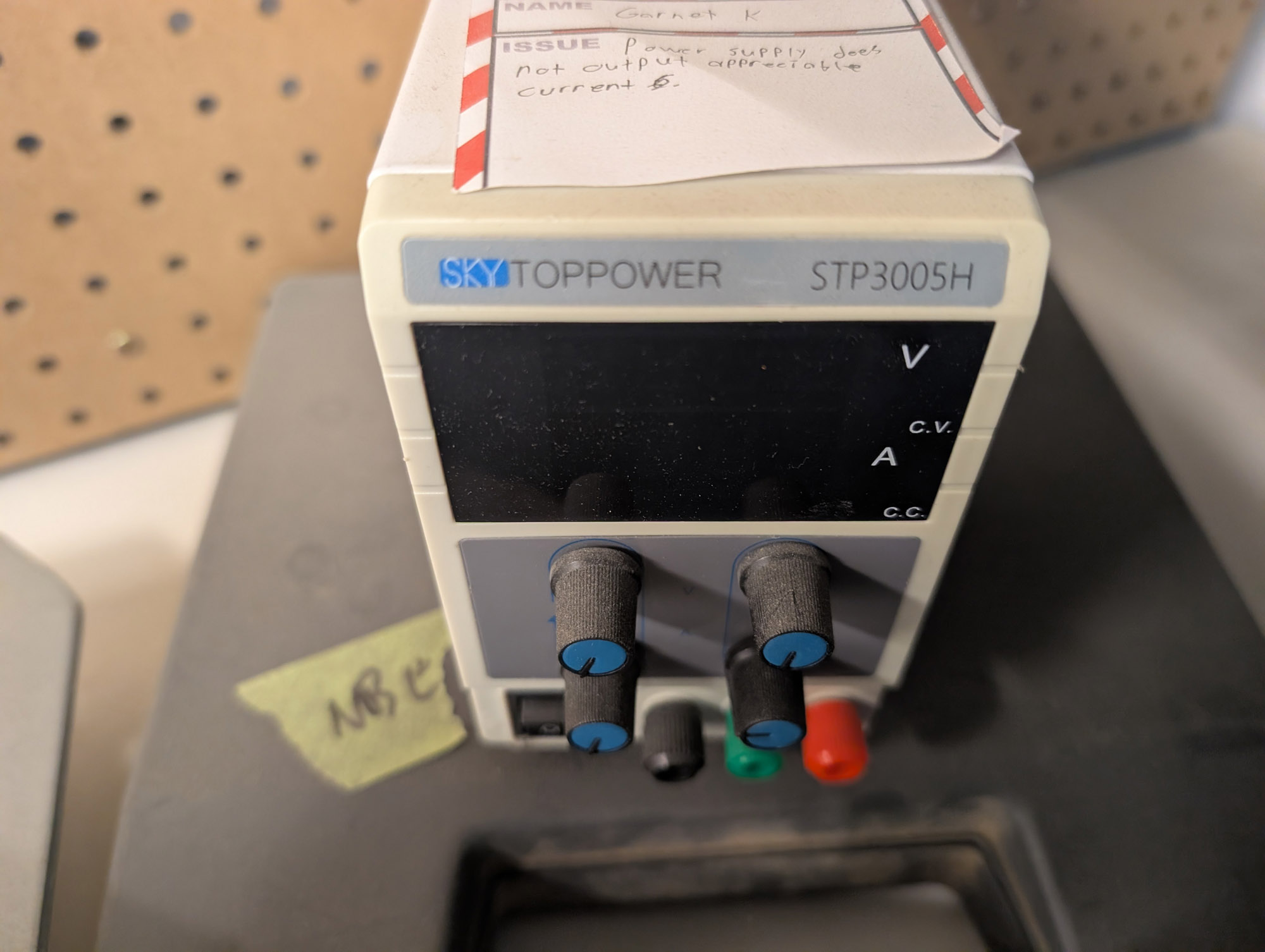A beige power supply with SKYTOPPOWER STP3005H across the top. A black display area is below that with displays for V and A, and LEDs for CV and CC. Four knobs are below that with legends not visible in the photo, as well as a power rocker switch, and black green and red combo banana jack/binding posts. A Kwartzlab out-of-order tag is on top from Garnet K saying "power supply does not output appreciable current".